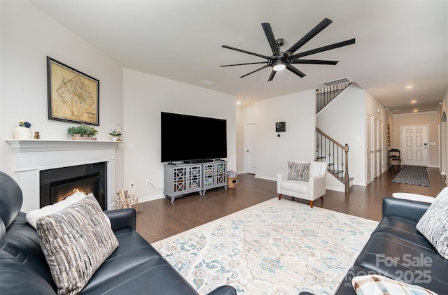 living area featuring baseboards, visible vents, a glass covered fireplace, dark wood-type flooring, and stairs