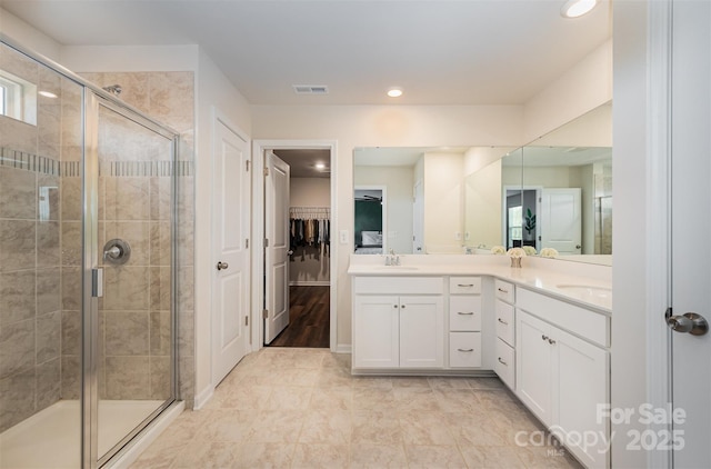 full bathroom with double vanity, a shower stall, a spacious closet, and visible vents