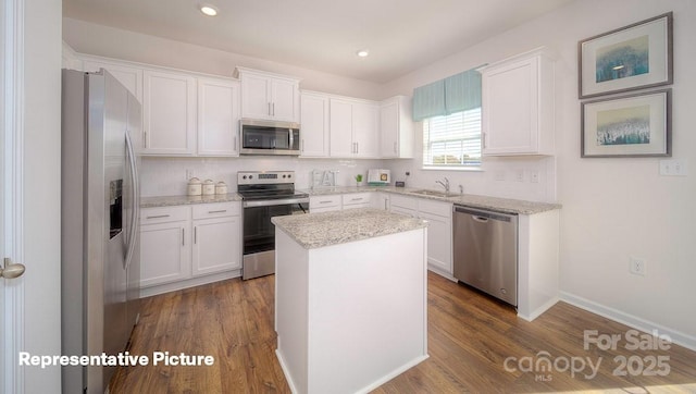 kitchen with appliances with stainless steel finishes, white cabinetry, backsplash, a center island, and light stone countertops