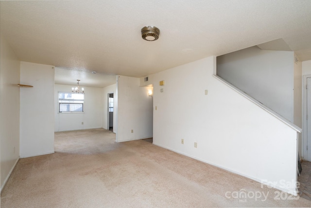 spare room featuring light colored carpet, a notable chandelier, a textured ceiling, and baseboards