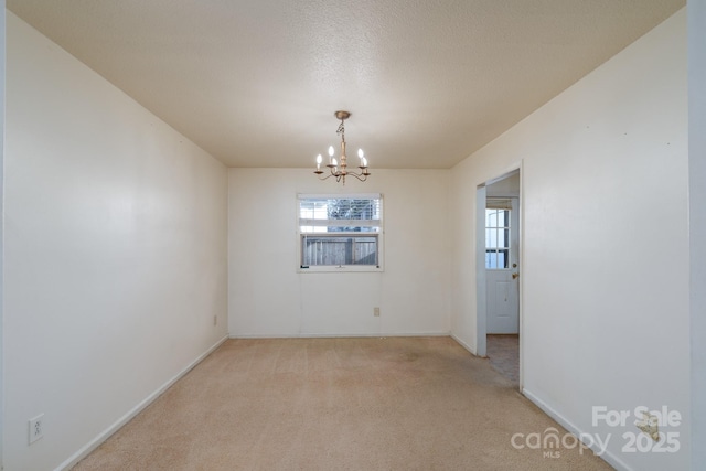 spare room featuring light colored carpet, a notable chandelier, baseboards, and a textured ceiling