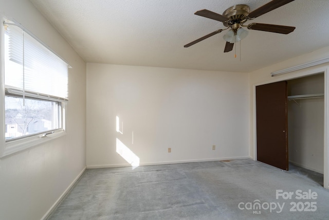 unfurnished bedroom featuring baseboards, a textured ceiling, ceiling fan, light carpet, and a closet