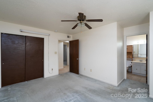 unfurnished bedroom featuring ensuite bathroom, light colored carpet, a textured ceiling, and visible vents