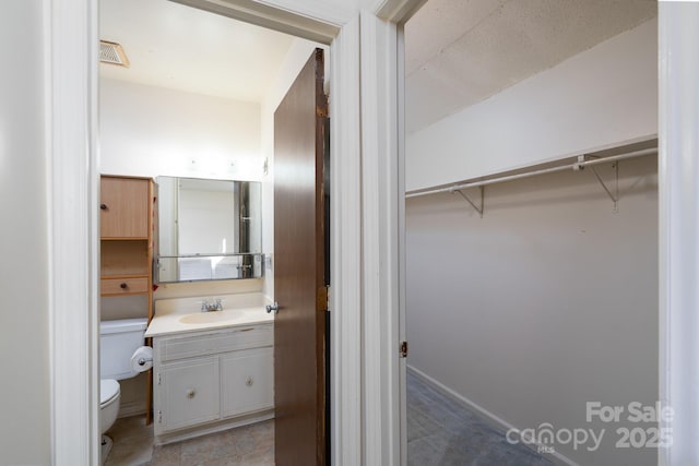 bathroom with toilet, a walk in closet, vanity, and visible vents