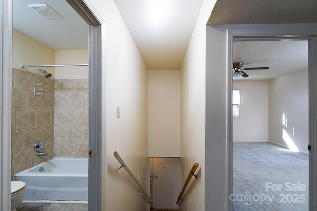 full bathroom with shower / washtub combination, toilet, visible vents, a ceiling fan, and a textured ceiling