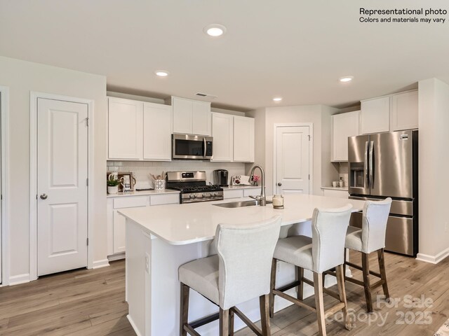 kitchen featuring stainless steel appliances, sink, a center island with sink, and white cabinets