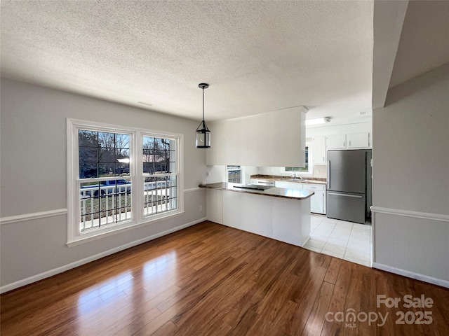 kitchen with light hardwood / wood-style flooring, stainless steel fridge, kitchen peninsula, pendant lighting, and white cabinets