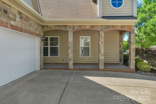 property entrance featuring roof with shingles, a porch, driveway, and stone siding