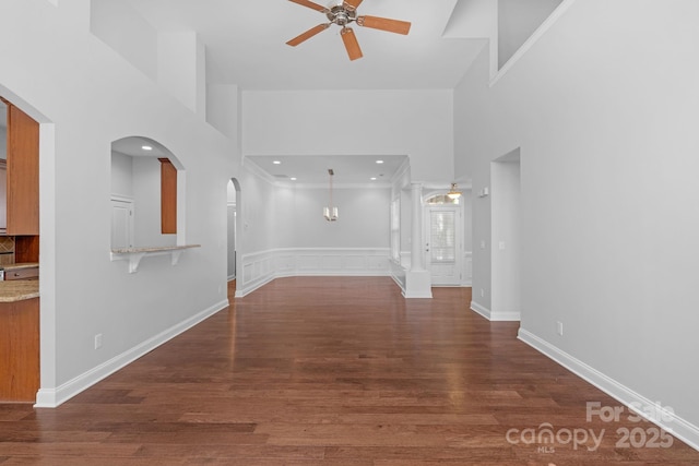 spare room featuring a ceiling fan, a towering ceiling, arched walkways, wood finished floors, and baseboards
