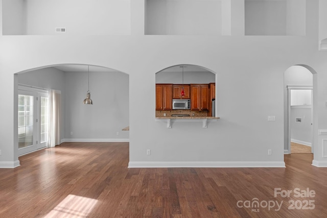 unfurnished living room with dark wood-style floors, a towering ceiling, and baseboards