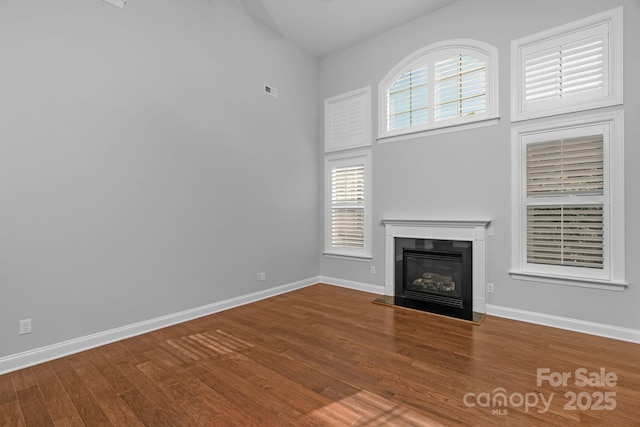 unfurnished living room with a glass covered fireplace, wood finished floors, baseboards, and a towering ceiling