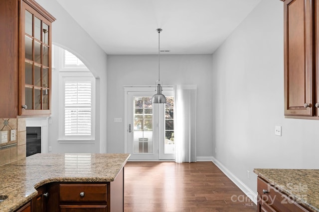 unfurnished dining area featuring dark wood-style floors, baseboards, a glass covered fireplace, and arched walkways