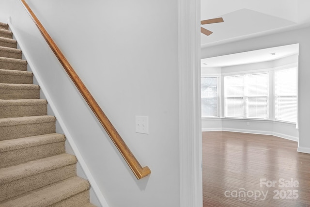 staircase with wood finished floors, ceiling fan, and baseboards