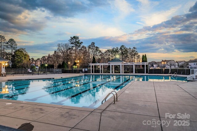 pool at dusk with fence, a community pool, and a patio area
