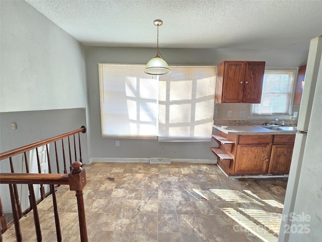 kitchen with tasteful backsplash, hanging light fixtures, sink, and a textured ceiling