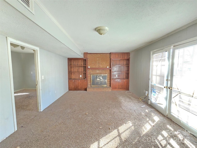 unfurnished living room featuring carpet floors, a textured ceiling, a brick fireplace, built in shelves, and french doors