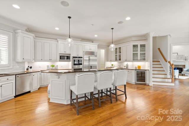 kitchen featuring built in appliances, a breakfast bar area, beverage cooler, white cabinets, and dark countertops