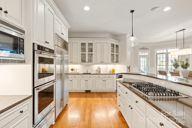 kitchen with light wood-type flooring, hanging light fixtures, backsplash, and built in appliances