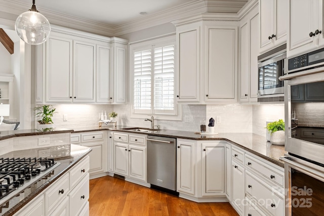 kitchen with appliances with stainless steel finishes, white cabinets, dark stone counters, a sink, and light wood-type flooring