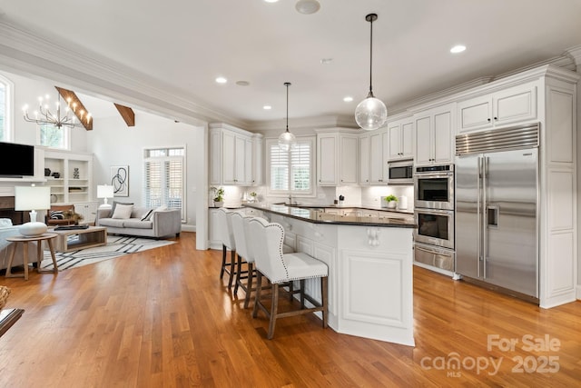 kitchen featuring built in appliances, a breakfast bar, open floor plan, a warming drawer, and dark countertops