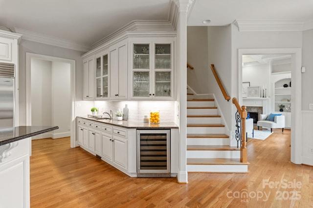 bar featuring built in shelves, light wood-type flooring, beverage cooler, and crown molding