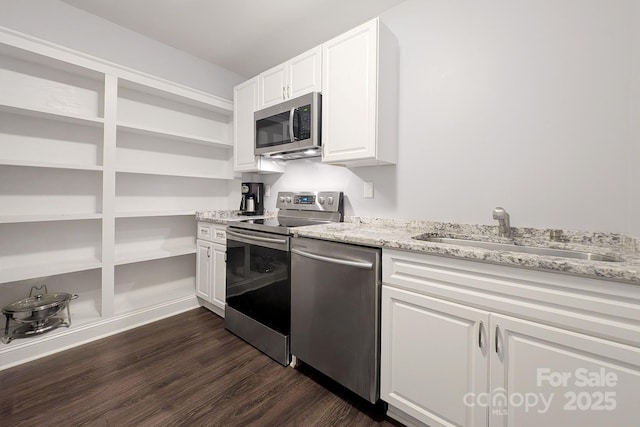 kitchen with white cabinets, dark wood-style floors, light stone countertops, stainless steel appliances, and a sink