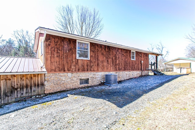 view of side of property featuring stone siding, central AC, and metal roof