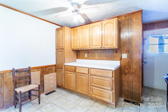 kitchen with a wainscoted wall, light countertops, visible vents, a ceiling fan, and wooden walls