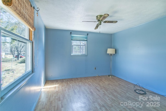 spare room with light wood-type flooring, baseboards, a ceiling fan, and a textured ceiling