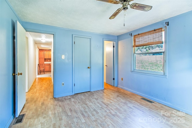 unfurnished bedroom with a textured ceiling, light wood finished floors, visible vents, and baseboards