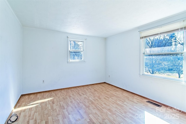 spare room featuring a textured ceiling, light wood-type flooring, visible vents, and baseboards