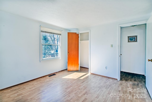 unfurnished bedroom with a closet, light wood-type flooring, visible vents, and baseboards