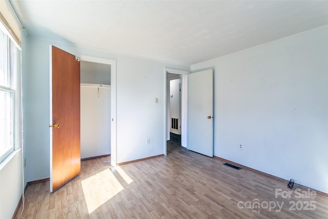 unfurnished bedroom with light wood-style flooring, multiple windows, and visible vents