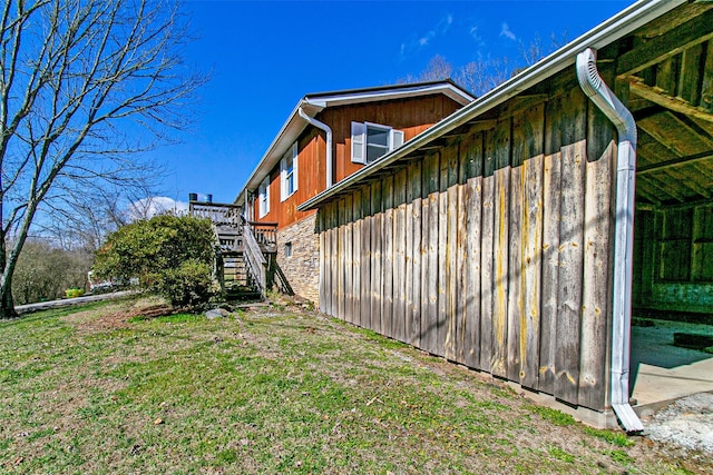 view of side of property with stone siding, a lawn, and stairs