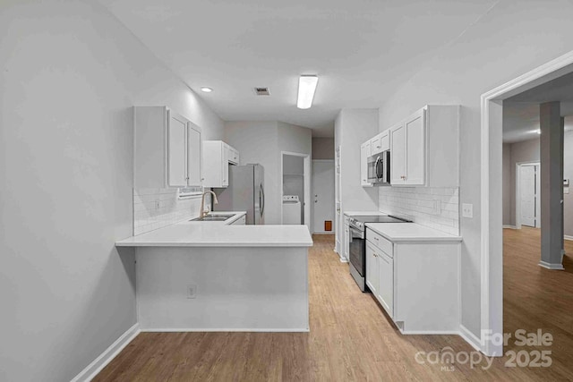 kitchen with sink, appliances with stainless steel finishes, white cabinets, washer / clothes dryer, and kitchen peninsula