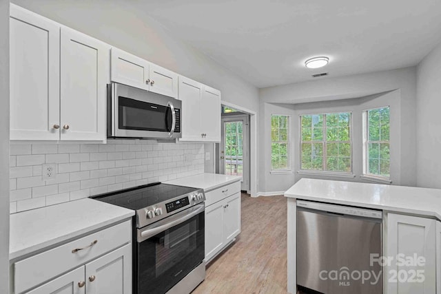 kitchen with white cabinetry, appliances with stainless steel finishes, light wood-type flooring, and backsplash