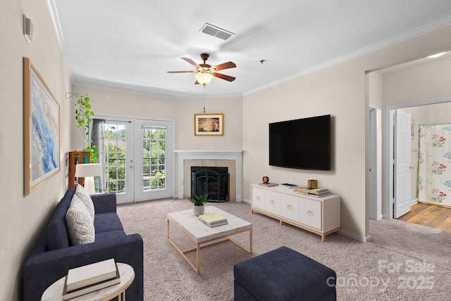 carpeted living room with crown molding, ceiling fan, and a tiled fireplace