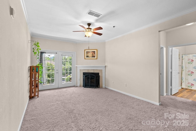 unfurnished living room featuring a tiled fireplace, crown molding, light colored carpet, and ceiling fan