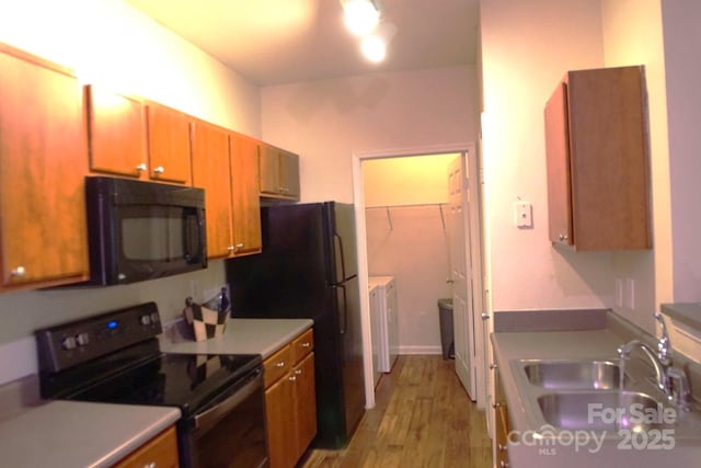 kitchen featuring sink, black appliances, independent washer and dryer, and light wood-type flooring