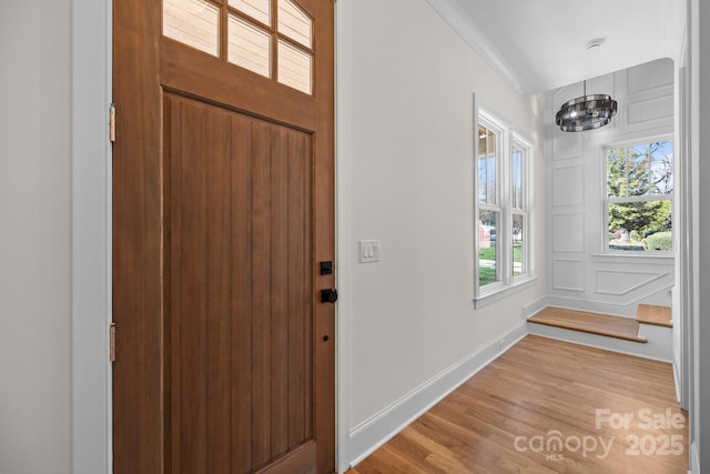 foyer entrance featuring baseboards, light wood-style floors, a chandelier, and a decorative wall