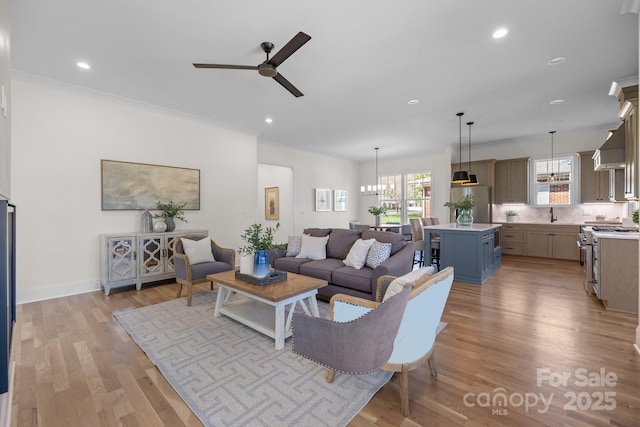 living room with baseboards, recessed lighting, crown molding, ceiling fan with notable chandelier, and light wood-type flooring