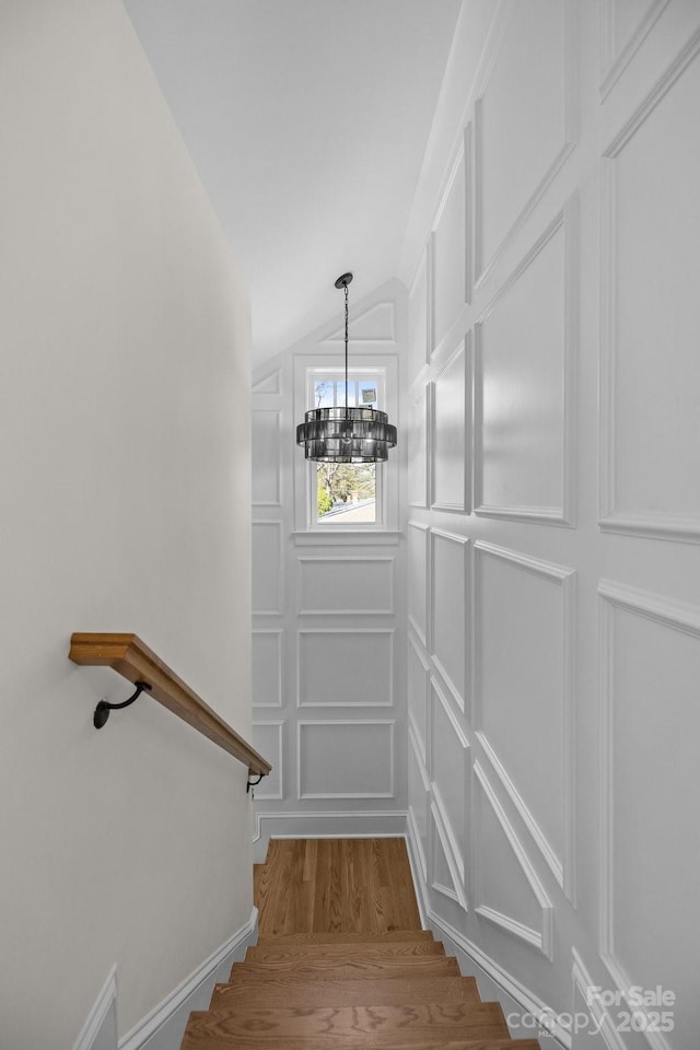 stairs featuring a notable chandelier, a decorative wall, vaulted ceiling, and wood finished floors