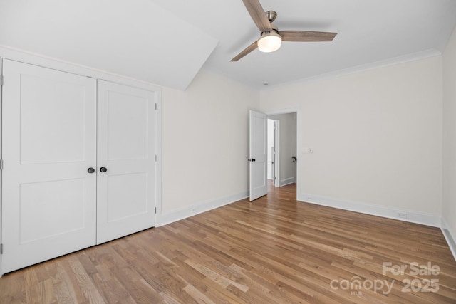 unfurnished bedroom with a ceiling fan, baseboards, light wood-style floors, a closet, and crown molding