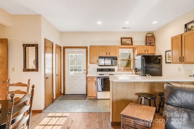 kitchen with a breakfast bar area, black appliances, a textured ceiling, and light wood-type flooring