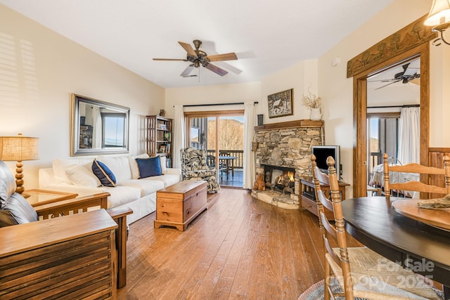 living room featuring hardwood / wood-style floors, a stone fireplace, and ceiling fan