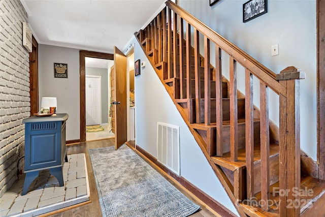 stairs featuring baseboards, visible vents, brick wall, and wood finished floors