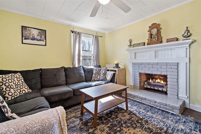 living area with a fireplace, a ceiling fan, baseboards, dark wood-style floors, and crown molding