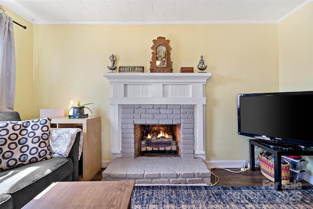 living area featuring ornamental molding, a brick fireplace, wood finished floors, and baseboards