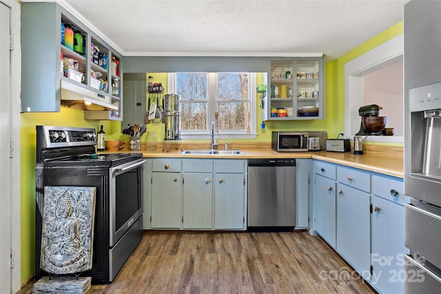 kitchen featuring stainless steel appliances, a sink, light countertops, open shelves, and dark wood finished floors