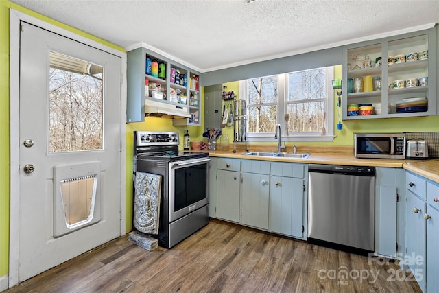 kitchen featuring dark wood finished floors, stainless steel appliances, light countertops, a sink, and under cabinet range hood